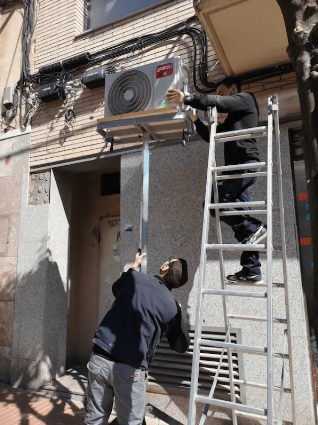 Dos instaladores colocando la unidad exterior de un aire acondicionado en una fachada
